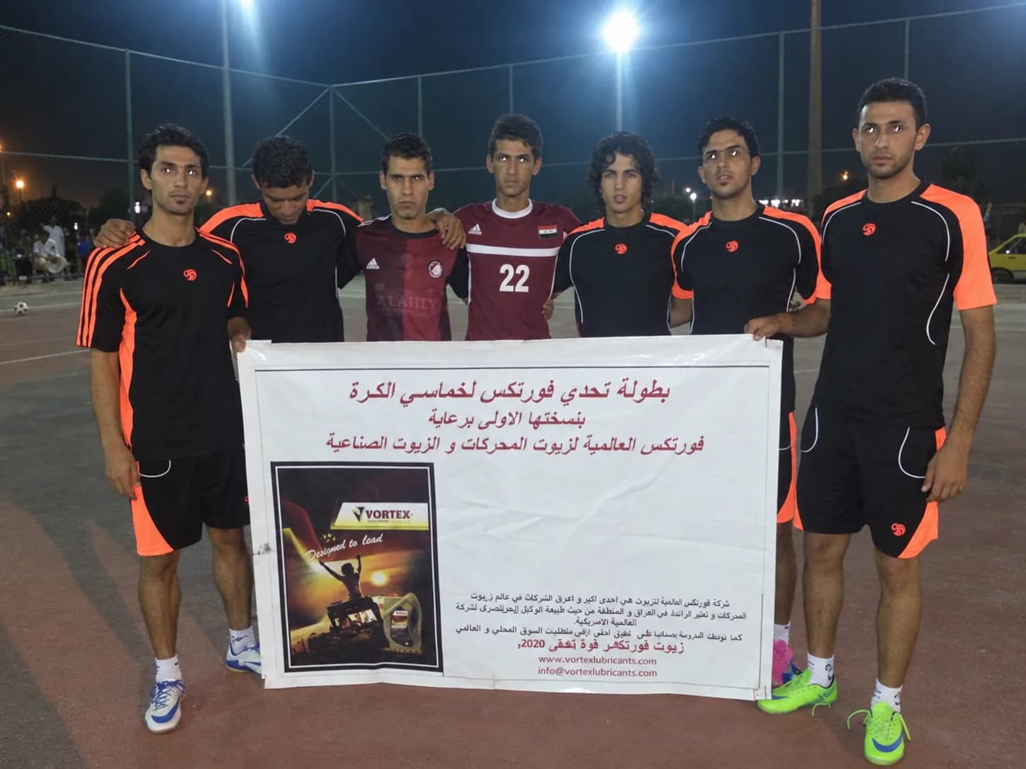 A team in black and orange holding the tournament banner under the floodlights