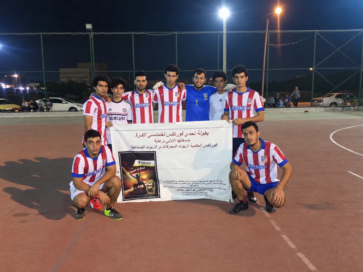A team in red and white stripes behind the tournament banner, two players kneeling at the front