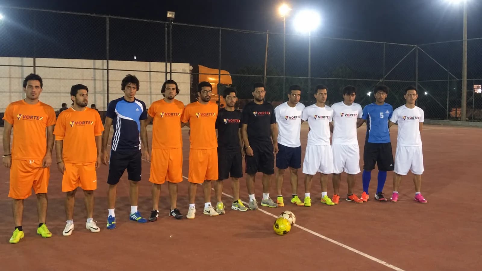 Two teams lined up across the pitch before kick-off, one side in orange Vortex shirts, the ball on the centre spot