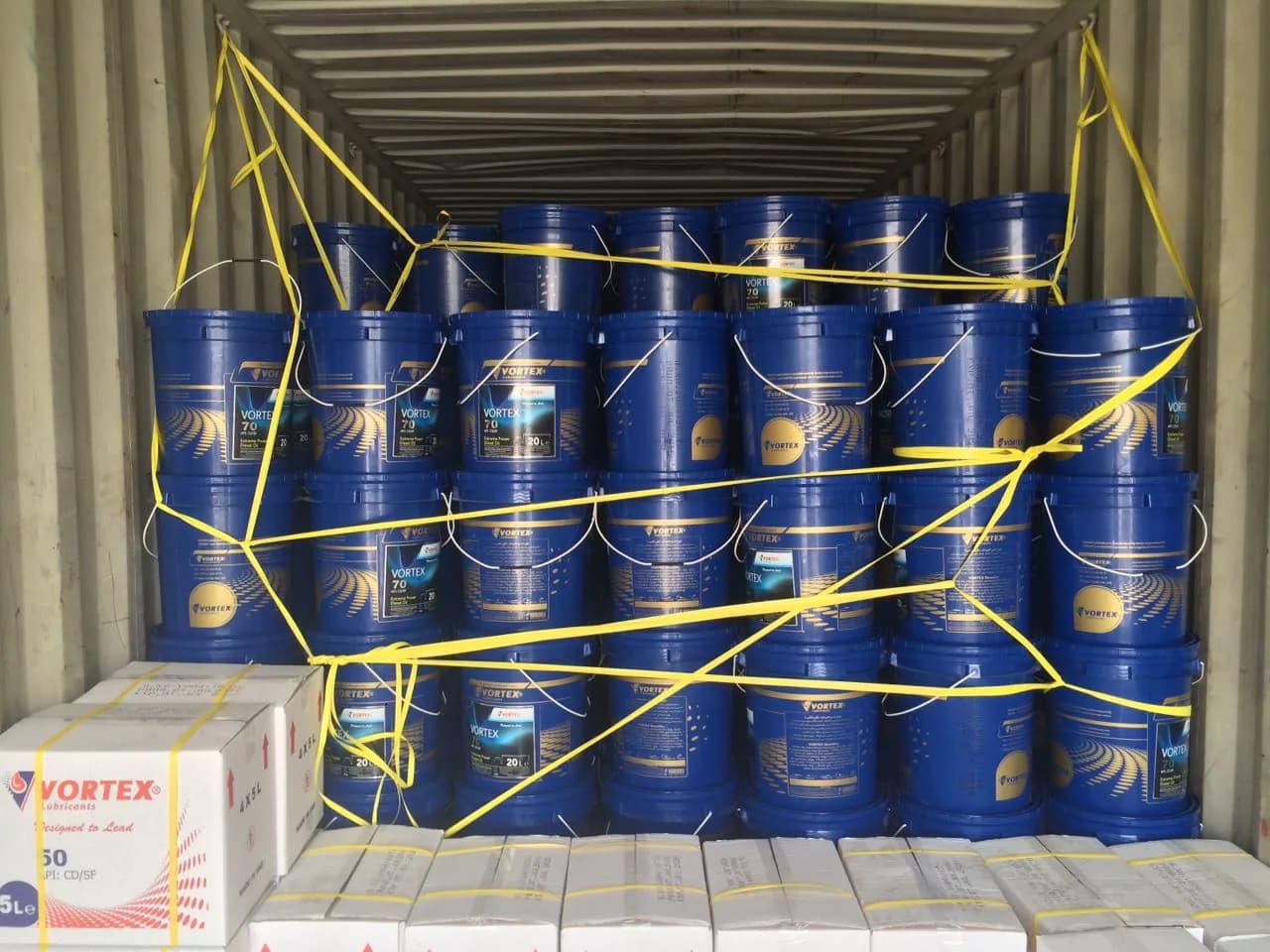 Sea container loaded with navy Vortex twenty-litre pails and export cartons, secured with yellow strapping