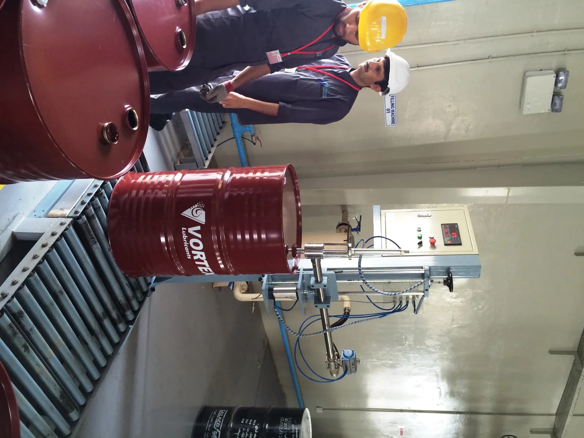Two operators in hard hats filling an oxblood Vortex drum on a roller conveyor