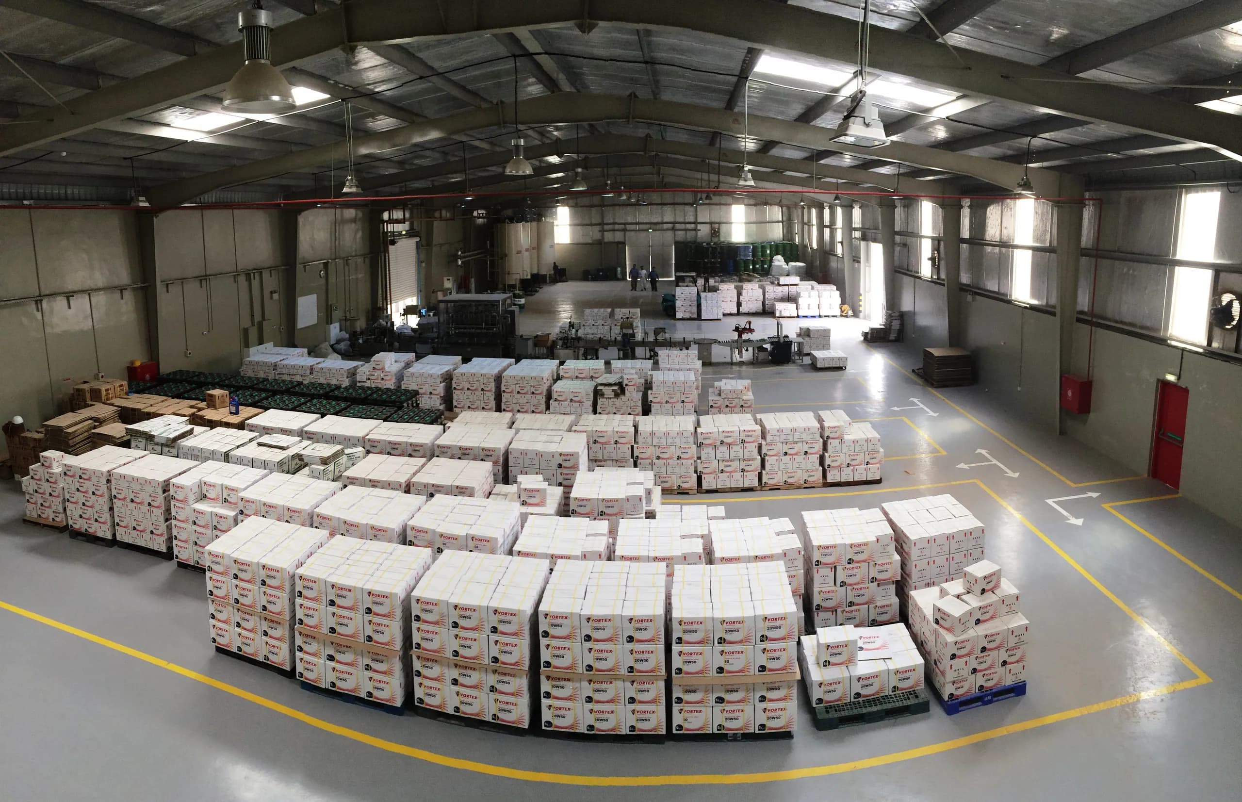 Elevated view across the warehouse floor, rows of palletised Vortex cartons stretching to the filling line at the far wall